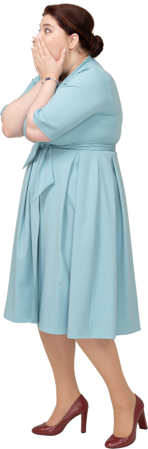 Vista lateral de una mujer impresionada en vestido azul cubriendo la boca con las manos
