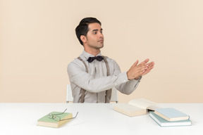 Jeune professeur assis à la table avec des livres dessus et applaudissant