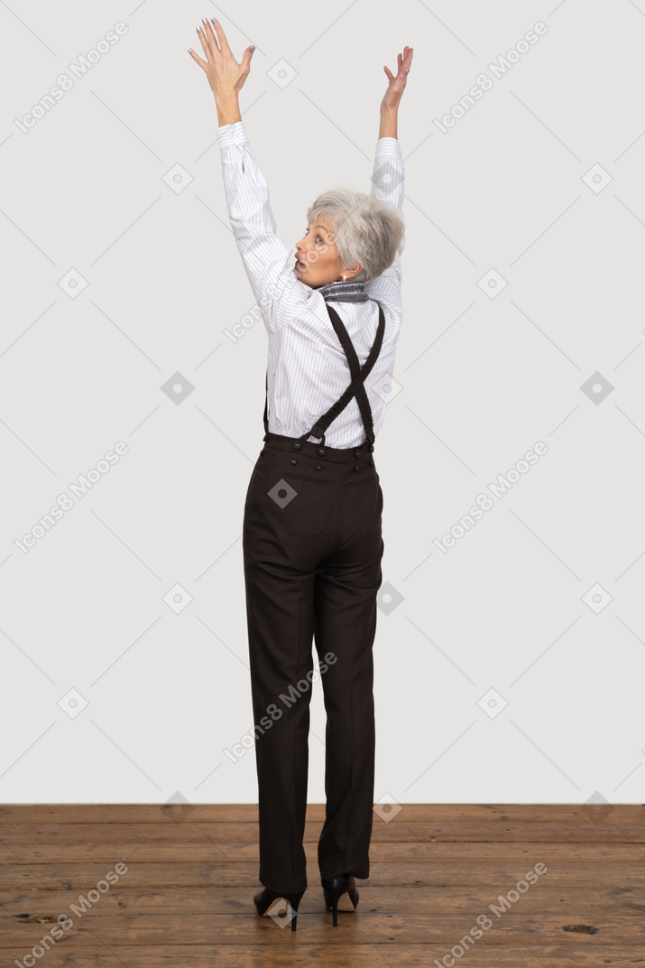 Vista posteriore di tre quarti di una vecchia signora in abiti da ufficio alzando le mani