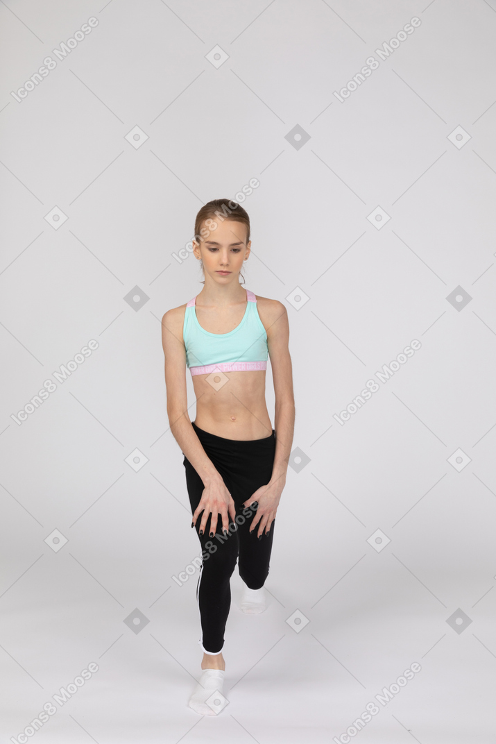 Vista frontal de uma adolescente em uma roupa esportiva fazendo uma estocada