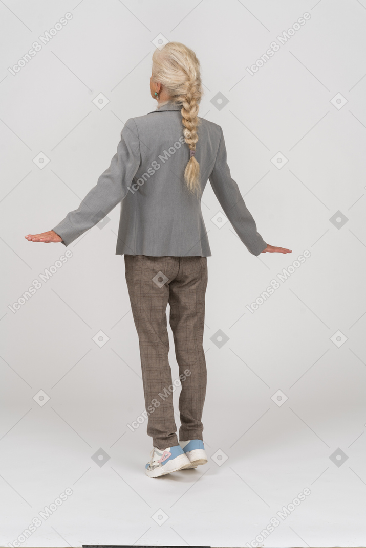 Vista traseira de uma senhora idosa de terno, na ponta dos pés e estendendo os braços
