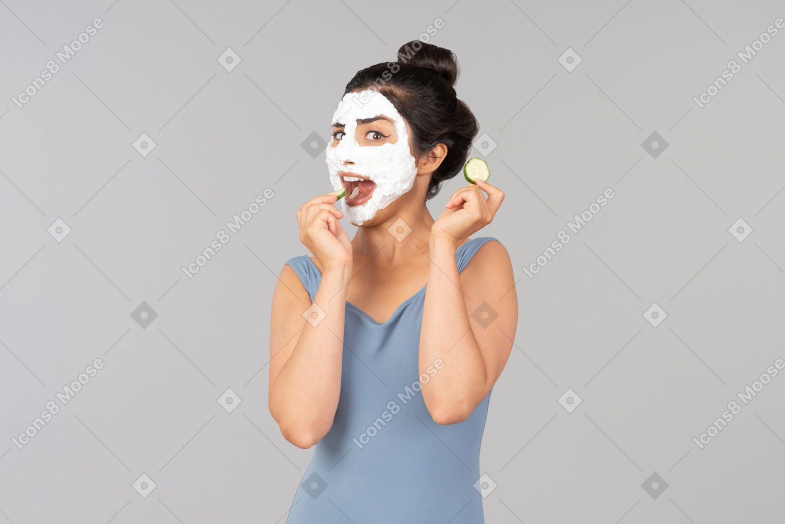 Young indian woman with white facial mask eating cucumber slices