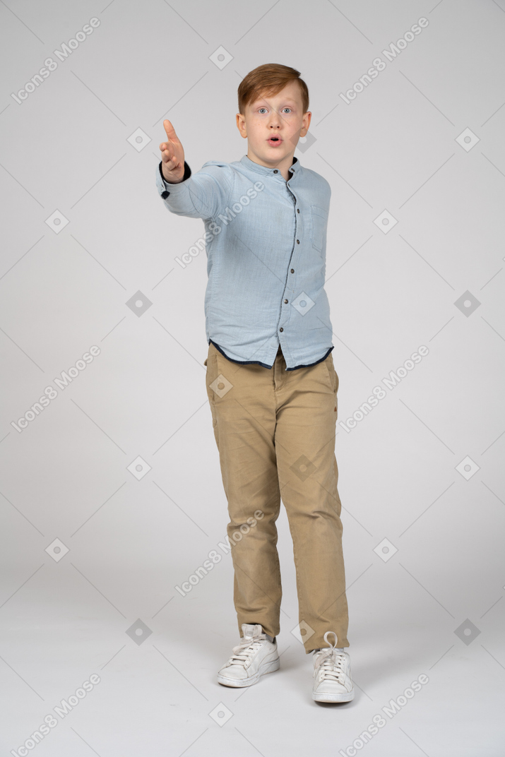 Front view of an impressed boy pointing at camera with hand