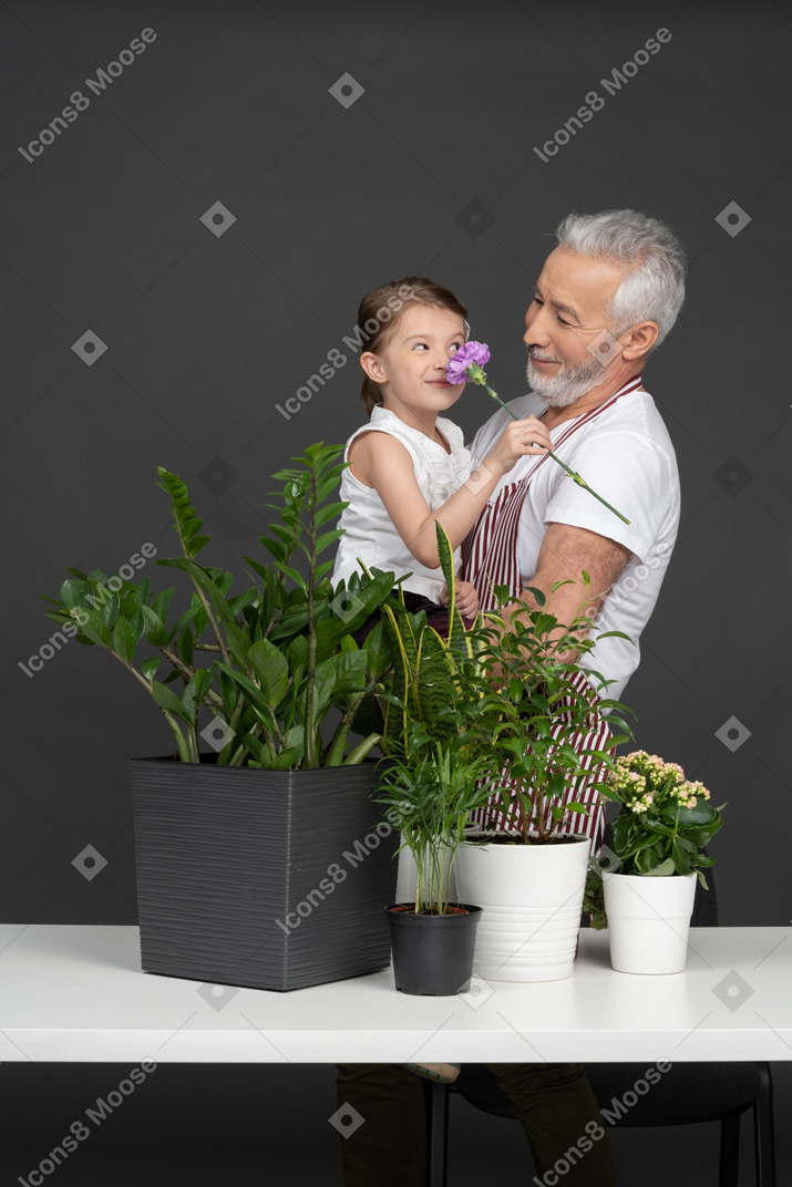 家の植物の横にある彼の手に小さな女の子を保持している成熟した男