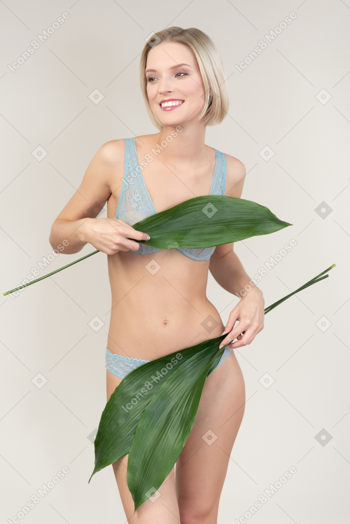 Sexy young woman closing her body with green leaves