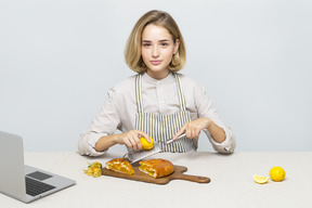 Chica atractiva cocinando una tarta de limón mientras ve un video en línea