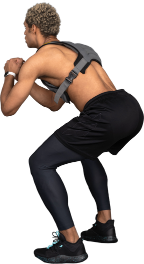 Vista posteriore di un uomo afro accovacciato a torso nudo