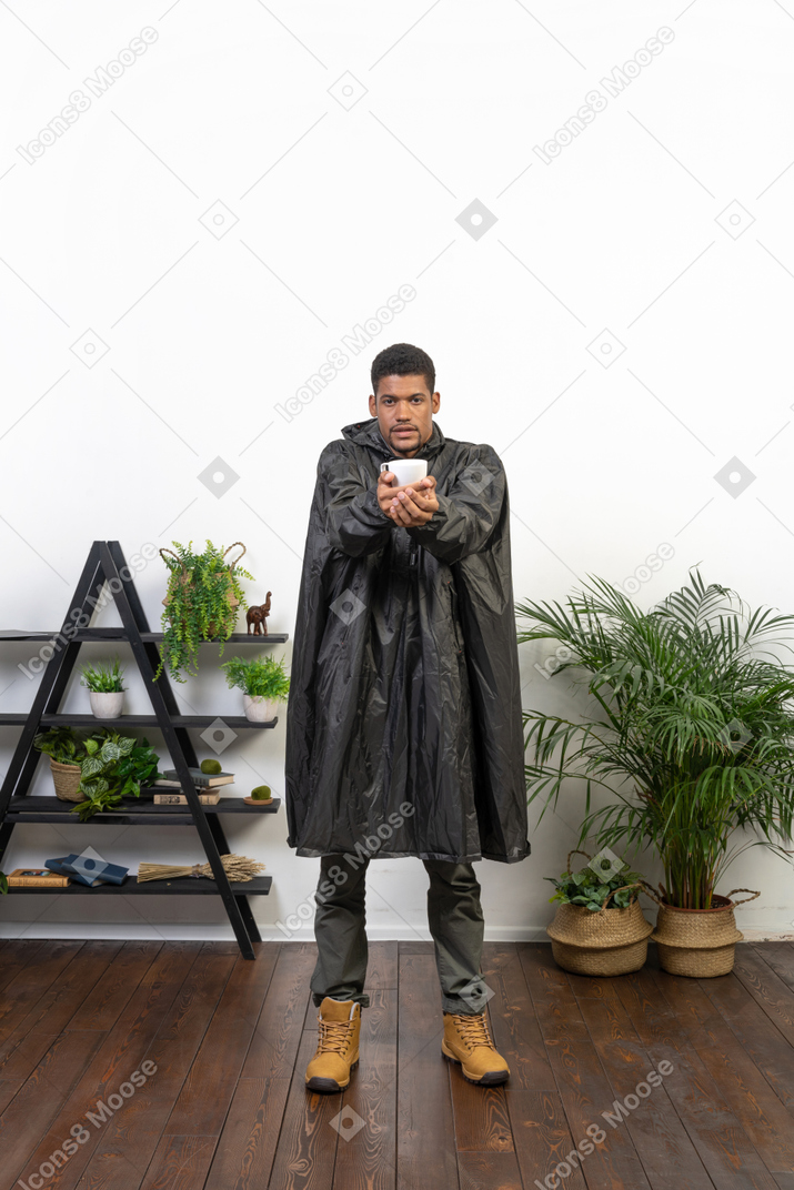 Homem de capa de chuva segurando uma xícara com os braços estendidos