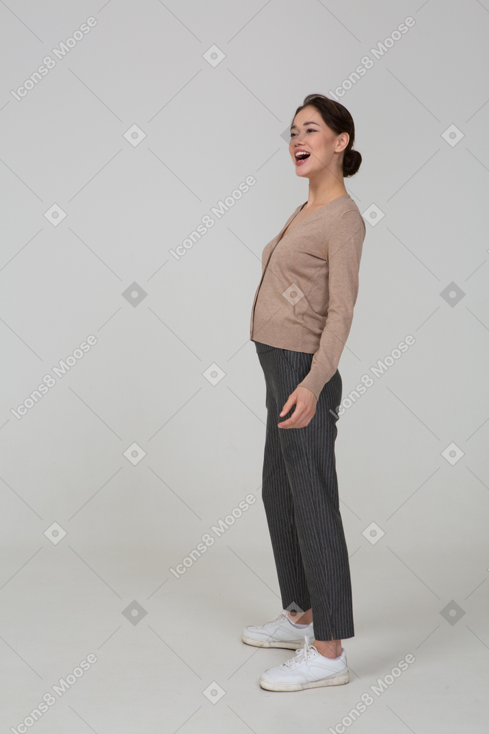 Three-quarter view of a laughing female in pullover and pants putting hand on hip