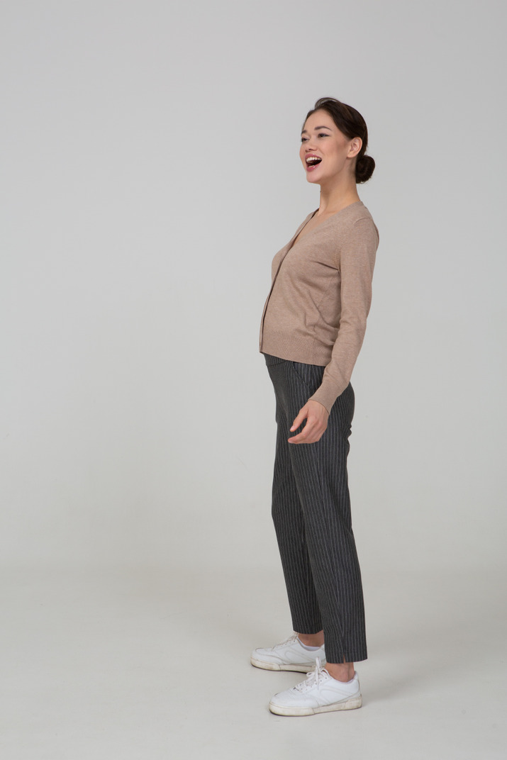 Three-quarter view of a laughing female in pullover and pants putting hand on hip