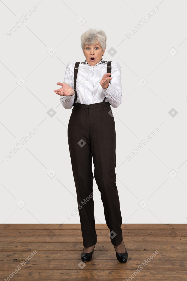 Front view of a surprised old lady in office clothing raising her hands