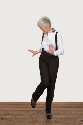 Front view of a careful old lady raising her leg while gesticulating