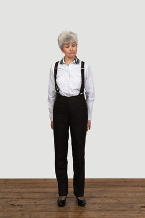 Vista frontal de uma velha envergonhada com roupas de escritório fazendo uma careta com as mãos atrás das costas