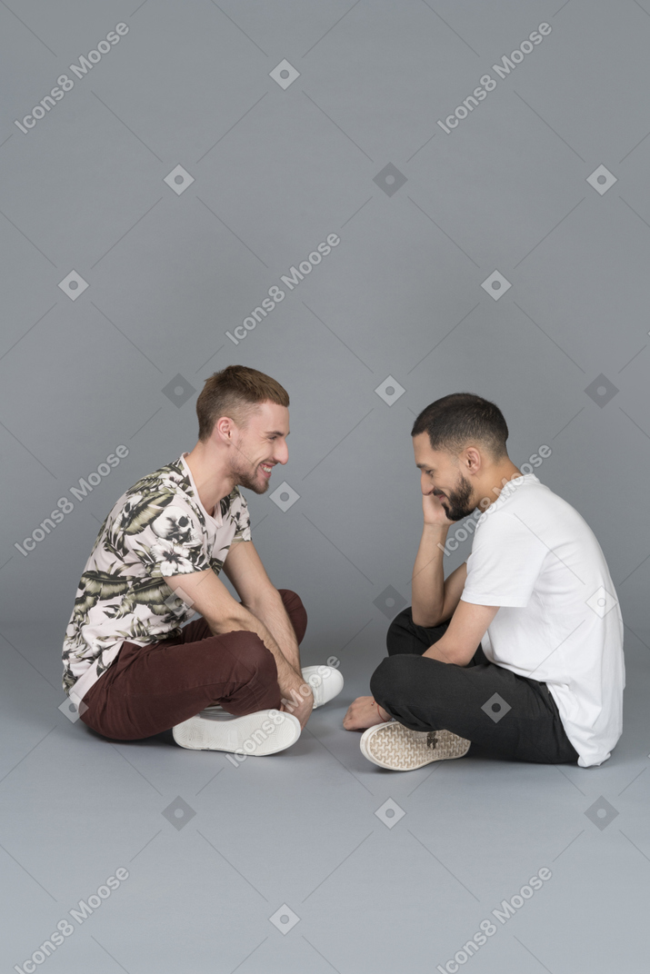 Side view of two happy young men sitting across from each other and smiling