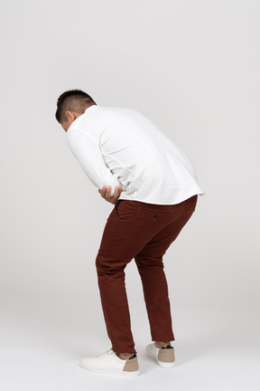 Three-quarter back view of a young latino man crouching and laughing hard