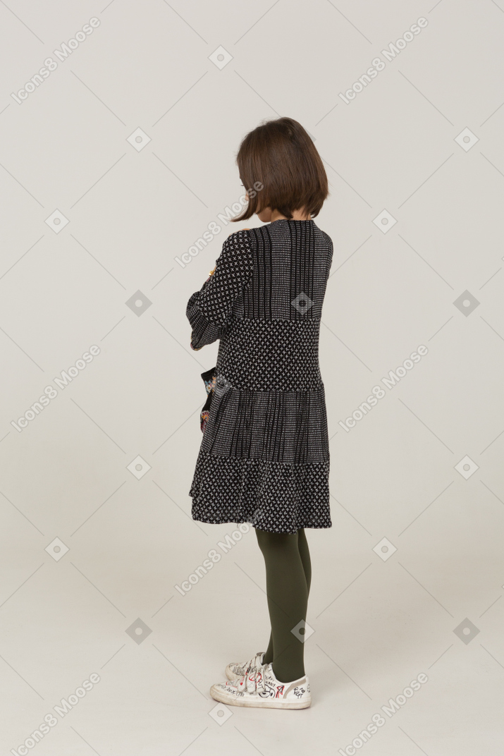 Three-quarter back view of an offended little girl in dress crossing arms
