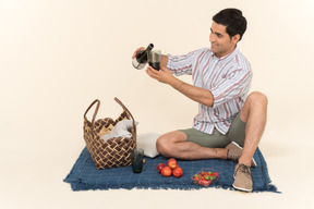 Young caucasian man sitting on the blanket and pouring wine into glass