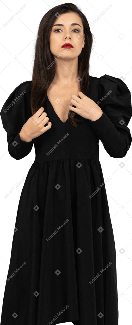 Front view of a serious young female adjusting her black dress