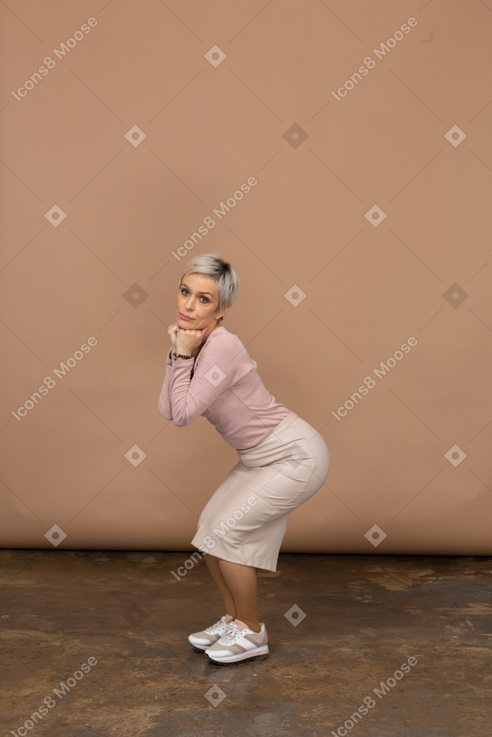 Side view of a woman in casual clothes squatting and making faces