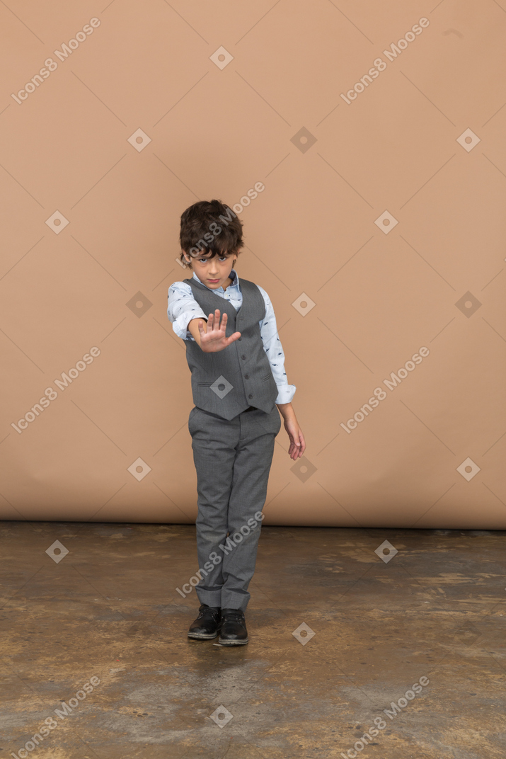 Вид спереди мальчика в сером костюме, показывающего стоп-жест