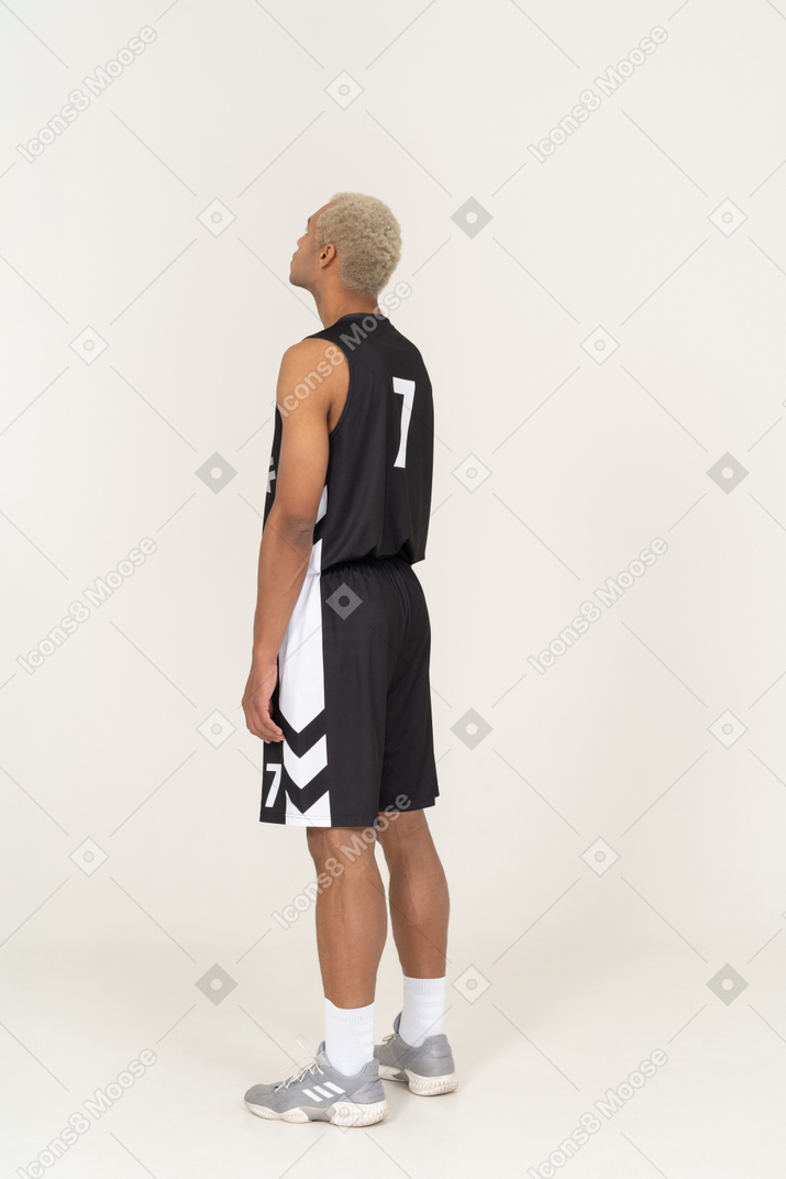 Vista posterior de tres cuartos de un joven jugador de baloncesto masculino mirando hacia arriba