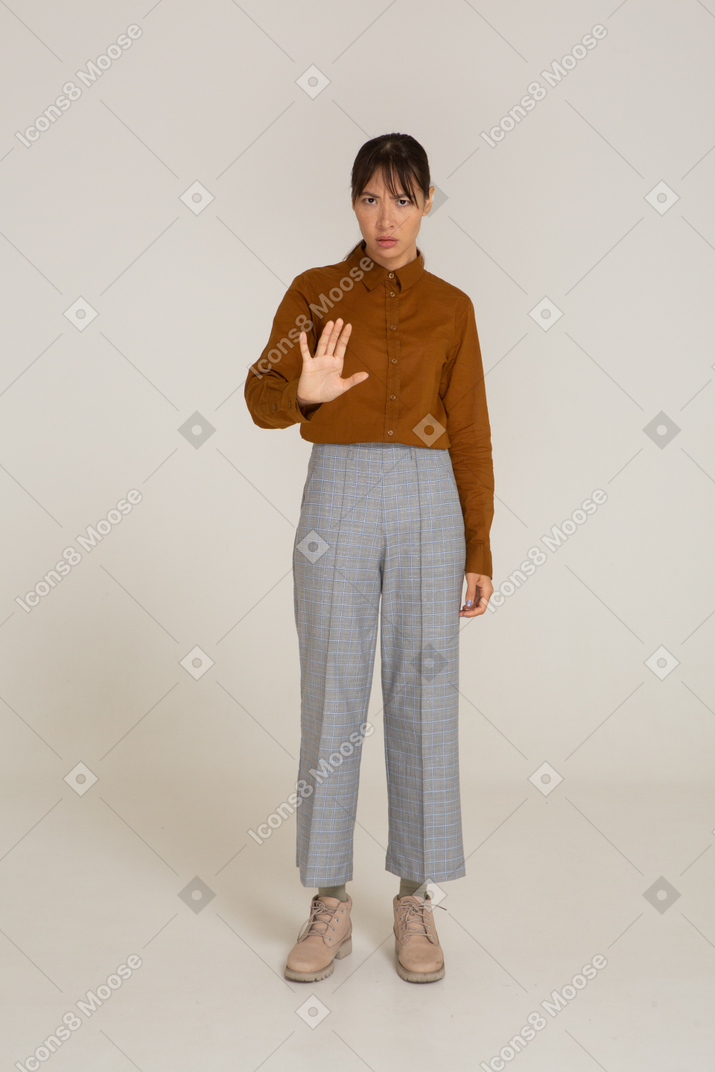 Vista frontal de uma jovem mulher asiática de calça e blusa esticando o braço