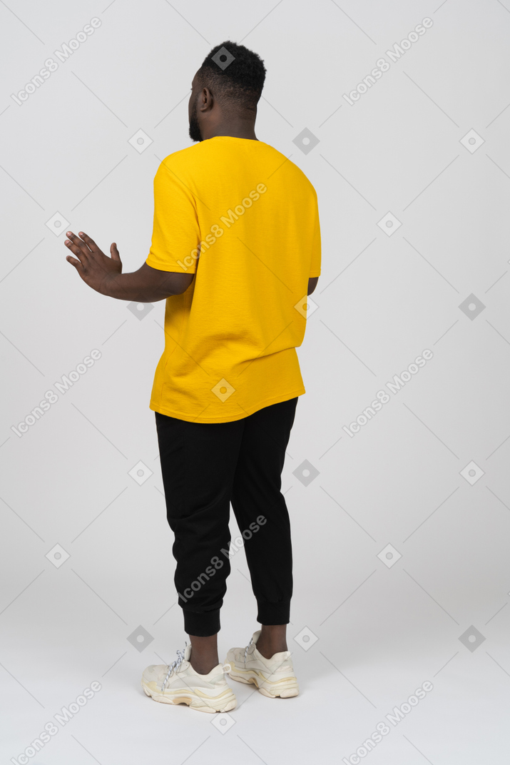 Три четверти сзади молодого темнокожего мужчины в желтой футболке, протягивающего руки