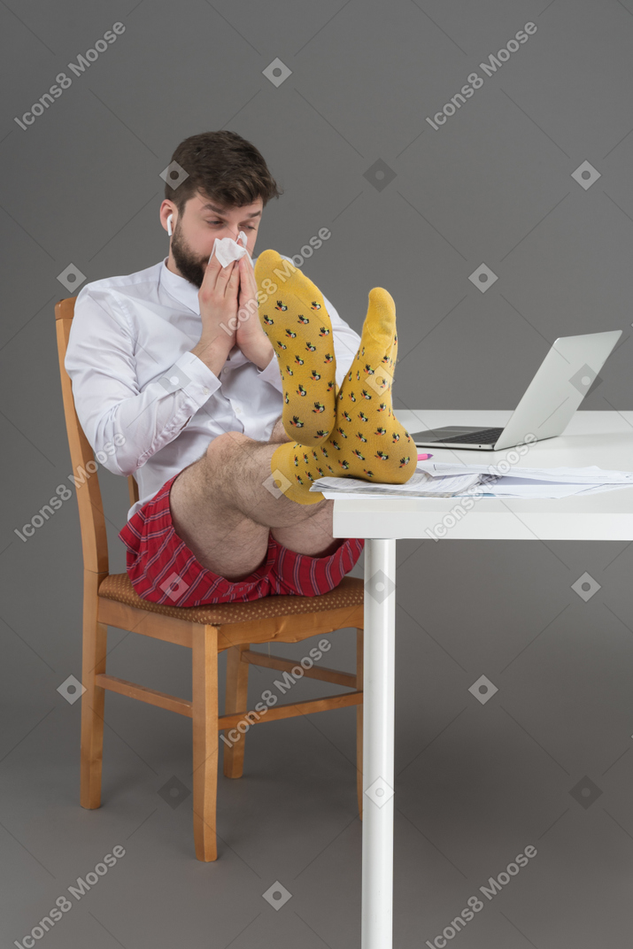Sick white collar worker wiping his nose and keeping his legs on the table