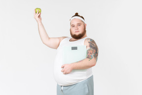 Young big guy in sportswear holding weights and apple