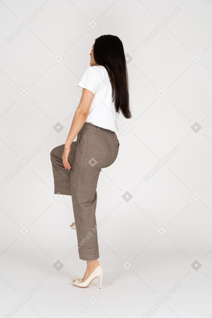 Three-quarter back view of young lady in breeches and t-shirt raising leg