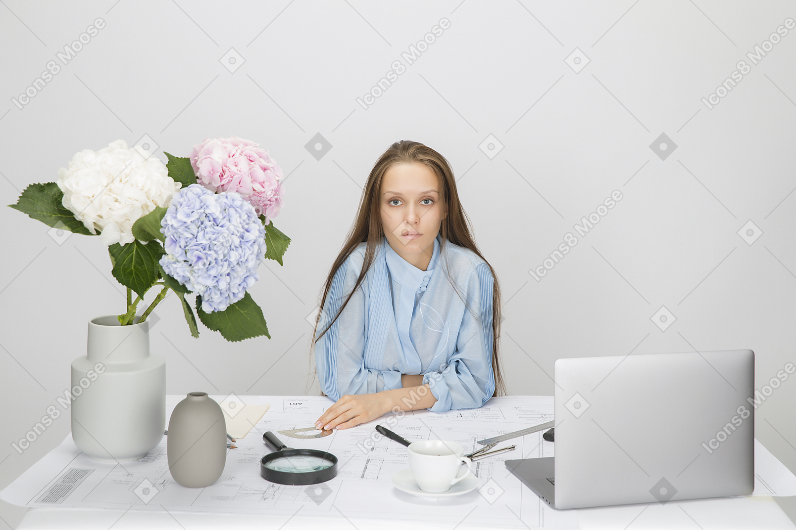 Young girl sitting at the table with laptop, coffee and vase with flowers