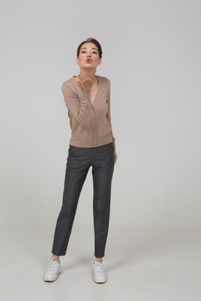 Front view of a young lady in pullover and pants sending an air kiss