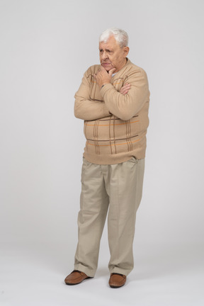 Vue de face d'un vieil homme pensif dans des vêtements décontractés debout avec la main sur le menton