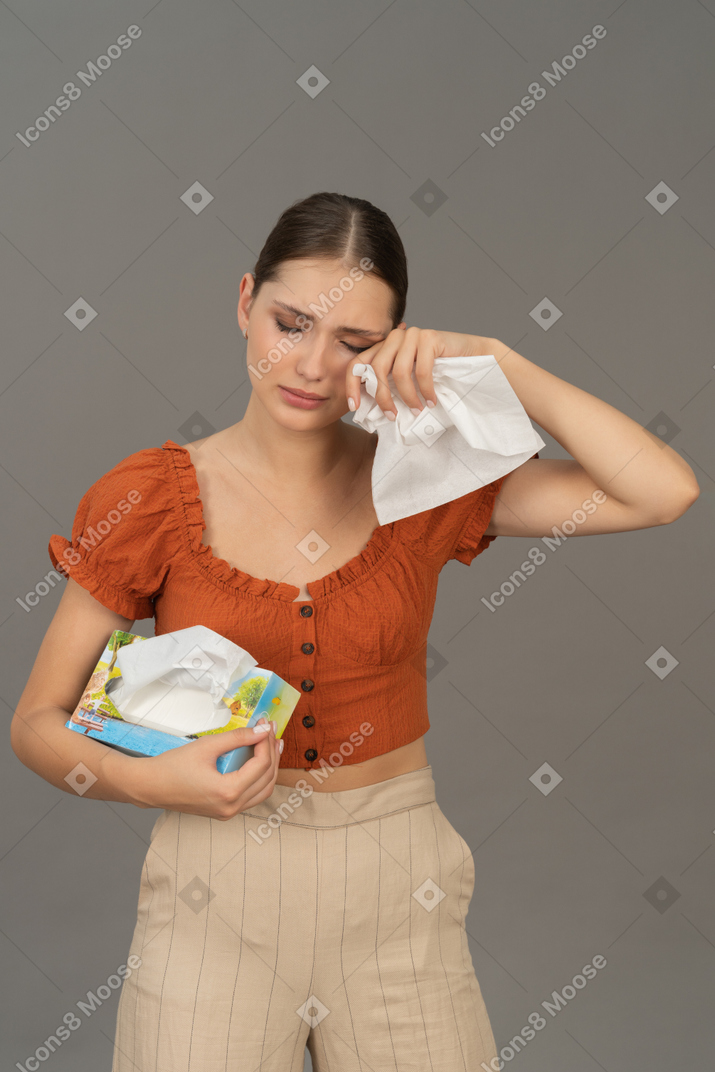 Front view of young woman crying with tissue in hands
