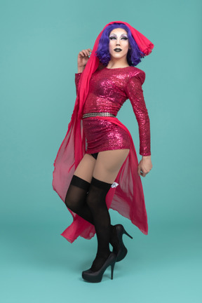 Vista lateral de una drag queen con vestido rosa levantando una falda larga hasta la cabeza