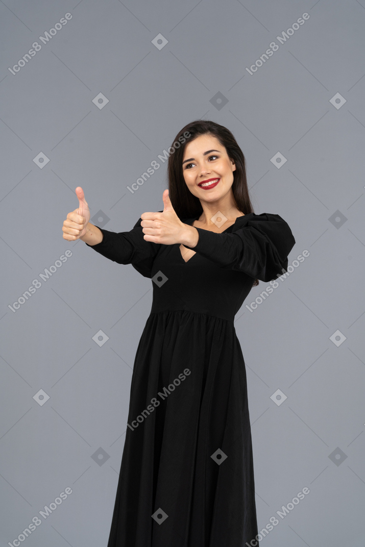 Vista di tre quarti di una giovane donna in un abito nero che mostra i pollici in su