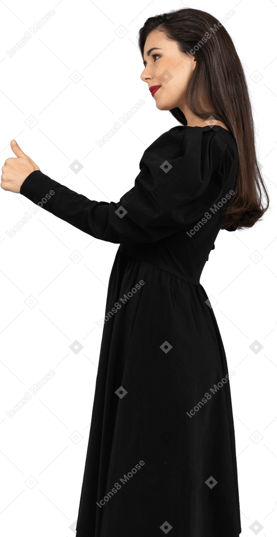 Вид сбоку улыбающейся молодой леди в черном платье показывает палец вверх