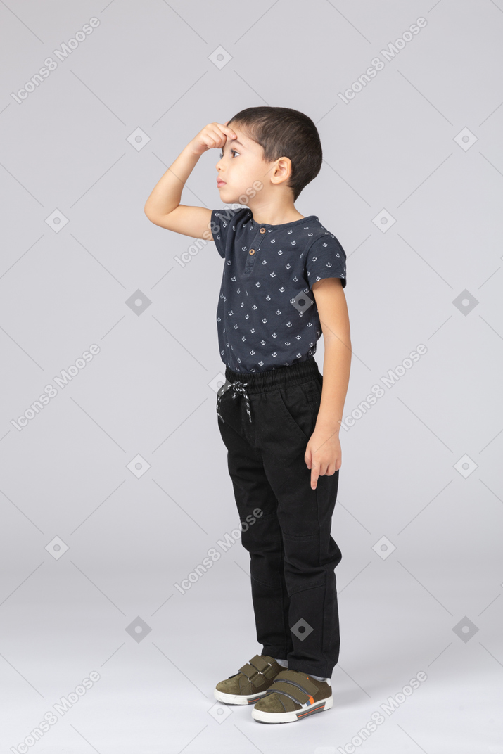 Side view of a cute boy in casual clothes pointing to forehead with finger