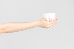 Mano femenina sosteniendo la taza de cerámica blanca