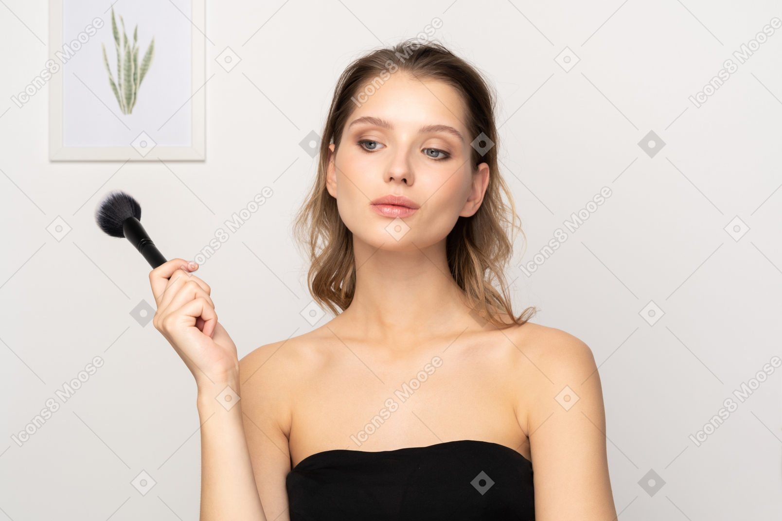 Vista frontal de uma jovem pensativa e sensual segurando um pincel de maquiagem