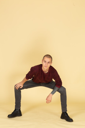 Front view of a squatting young man in red pullover