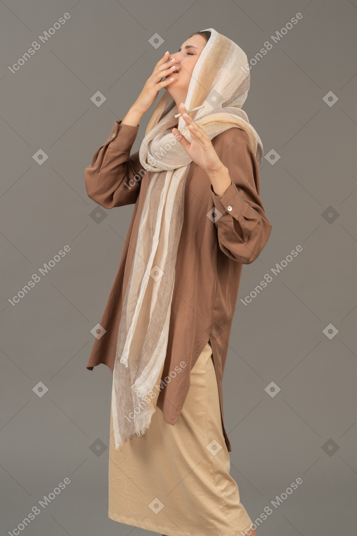 Young woman in headscarf coughing with cigarette in hand