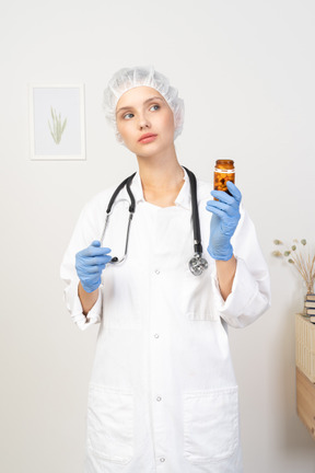 Front view of a young female doctor holding a jar of pills