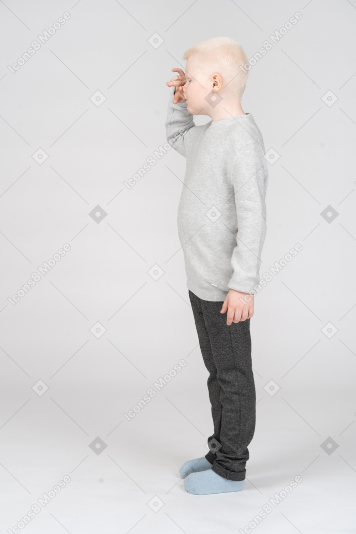 Vista laterale di un ragazzino che fa smorfie toccando il naso