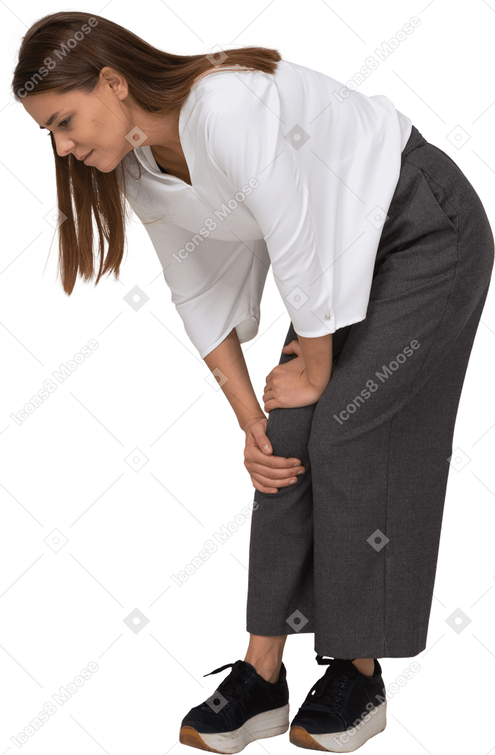 Vista di tre quarti di una giovane donna in abiti da ufficio che si piega e tocca il ginocchio