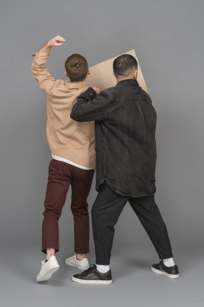 Vue arrière de deux jeunes hommes agités avec un panneau d'affichage et un poing levé