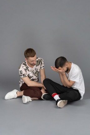 Young man sitting on the floor and listening to another distressed young man