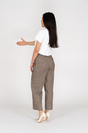 Three-quarter back view of a greeting young lady in breeches and t-shirt outstretching her hand