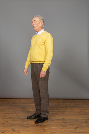 Vista di tre quarti di un vecchio sorpreso in pullover giallo che fa una smorfia e guarda da parte