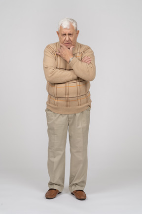 Vista frontal de un anciano pensativo con ropa informal de pie con la mano en la barbilla